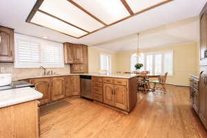 Kitchen featuring stainless steel dishwasher, kitchen peninsula, sink, a chandelier, and light wood-type flooring