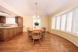 Dining area with crown molding, vaulted ceiling, a notable chandelier, and light hardwood / wood-style floors