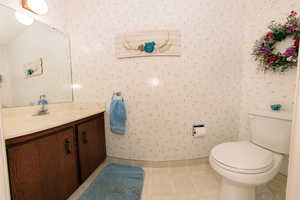 Bathroom off laundry  featuring vanity, toilet, vaulted ceiling, and tile patterned floors