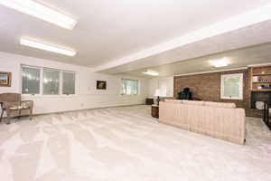 Living room with brick wall, light colored carpet, a healthy amount of sunlight, and a wood burning fireplace