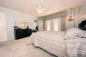 Primary carpeted bedroom featuring ceiling fan with notable chandelier and ornamental molding