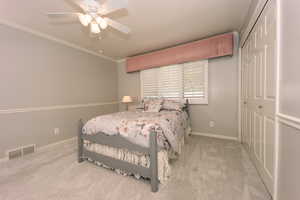 Bedroom featuring ceiling fan, ornamental molding, a closet, and light carpet