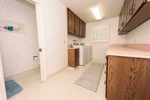 Clothes washing area featuring washing machine and clothes dryer and cabinets