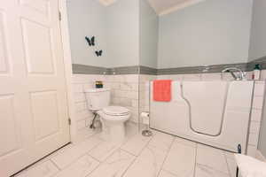 Main bathroom featuring ornamental molding, tile walls, toilet, and a bathtub