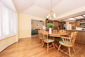 Dining space featuring light hardwood / wood-style flooring, ceiling fan with notable chandelier, crown molding, and vaulted ceiling