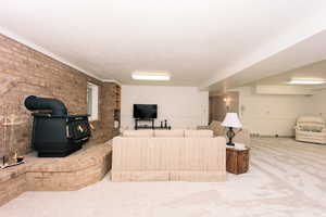 Carpeted living room featuring a wood stove, ornamental molding, and brick wall