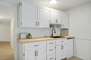 Kitchen featuring light wood-type flooring, wood counters, white cabinetry, and sink