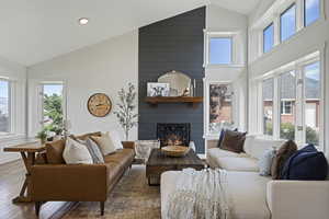 Living room featuring high vaulted ceiling, a large fireplace, wood-type flooring, and plenty of natural light