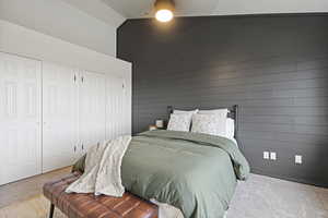 Bedroom featuring lofted ceiling, two closets, wood walls, and carpet floors