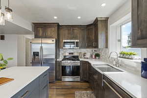 Kitchen with appliances with stainless steel finishes, dark hardwood / wood-style flooring, dark brown cabinets, and pendant lighting