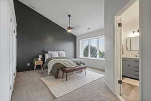 Bedroom with wooden walls, ceiling fan, vaulted ceiling, ensuite bathroom, and light hardwood / wood-style floors