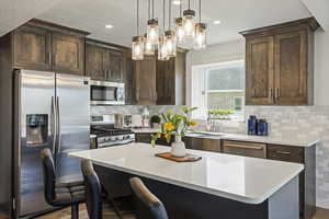 Kitchen featuring backsplash, decorative light fixtures, stainless steel appliances, a chandelier, and a kitchen island