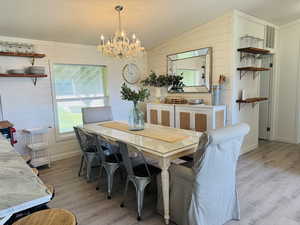 Dining room featuring vaulted ceiling, light wood-style flooring, a chandelier, and wood walls