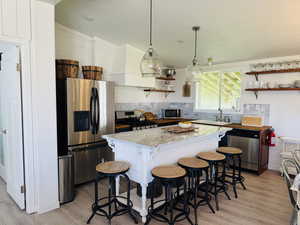 Kitchen with appliances with stainless steel finishes, open shelves, a center island, and light wood finished floors