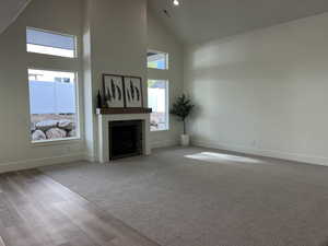 Unfurnished living room featuring visible vents, a brick fireplace, wood finished floors, high vaulted ceiling, and baseboards