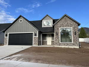 View of front facade with a garage, brick siding, a shingled roof, board and batten siding, and concrete driveway