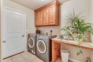 Washroom with light tile patterned floors, washing machine and clothes dryer, and cabinets