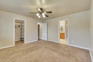 Primary bedroom featuring connected bathroom, ceiling fan, a closet, a spacious closet, and light colored carpet