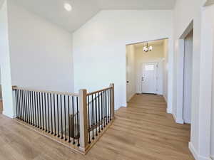 Hall featuring light wood-type flooring, high vaulted ceiling, and a chandelier