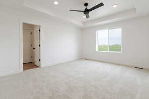 Unfurnished room with a raised ceiling, light carpet, and ceiling fan