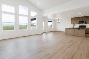 Unfurnished living room featuring sink, a chandelier, light hardwood / wood-style floors, and high vaulted ceiling