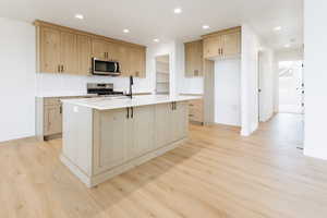 Kitchen with light hardwood / wood-style flooring, a center island with sink, appliances with stainless steel finishes, and light brown cabinetry