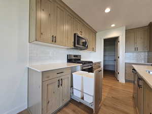 Kitchen with a textured ceiling, stainless steel appliances, light wood-type flooring, and decorative backsplash