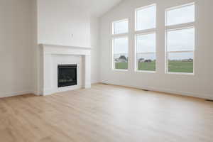 Unfurnished living room featuring light wood-type flooring and high vaulted ceiling