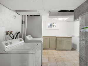 Clothes washing area with cabinets, independent washer and dryer, and light tile patterned flooring