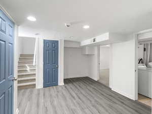 Basement with a textured ceiling, washing machine and dryer, and light hardwood / wood-style floors