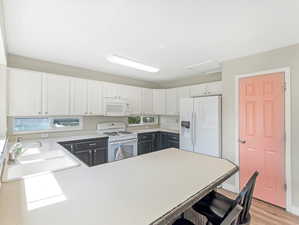 Kitchen with light wood-type flooring, white cabinetry, white appliances, a kitchen bar, and sink