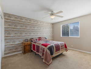 Carpeted bedroom with ceiling fan, wood walls, and a closet