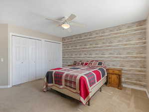 Bedroom featuring light colored carpet, ceiling fan, wood walls, and two closets