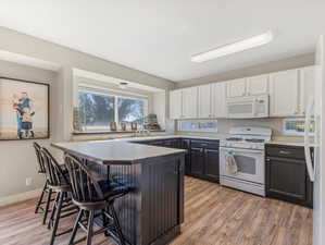 Kitchen featuring white appliances, a wealth of natural light, white cabinets, and a breakfast bar