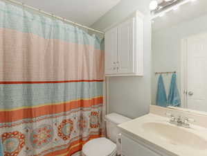 Bathroom featuring curtained shower, toilet, and vanity