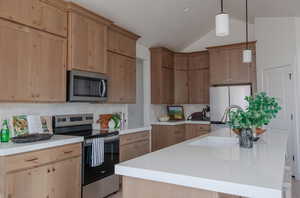 Kitchen with backsplash, lofted ceiling, stainless steel appliances, and an island with sink