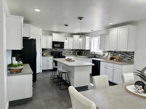 Kitchen featuring white cabinets, backsplash, decorative light fixtures, black appliances, and a kitchen island