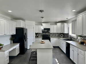 Spacious kitchen with white cabinetry, decorative light fixtures, black appliances, a kitchen island, and sink