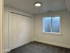 Sixth bedroom with a large window, dark colored carpet, and a closet