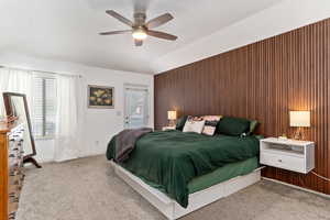 Bedroom featuring lofted ceiling, wood walls, ceiling fan, and light colored carpet