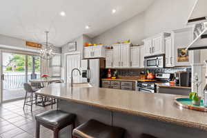 Kitchen featuring a notable chandelier, vaulted ceiling, sink, appliances with stainless steel finishes, and white cabinets