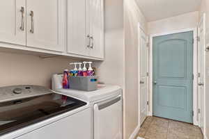 Clothes washing area with light tile patterned floors, cabinets, and washer and dryer