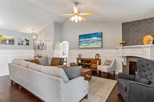 Living room featuring dark wood-type flooring, ceiling fan, high vaulted ceiling, and a fireplace