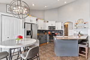 Kitchen featuring high vaulted ceiling, appliances with stainless steel finishes, a notable chandelier, and white cabinetry