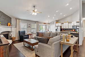 Living room with a stone fireplace, ceiling fan with notable chandelier, high vaulted ceiling, and dark hardwood / wood-style flooring