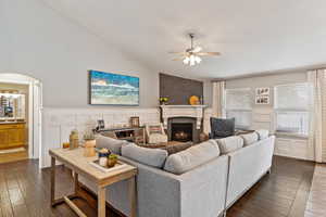 Living room with dark wood-type flooring, ceiling fan, a brick fireplace, and vaulted ceiling