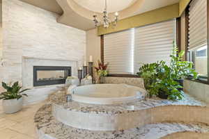 Full bath featuring an inviting chandelier, a fireplace, tile patterned flooring, and a jetted tub