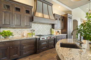 Kitchen featuring glass insert cabinets, stainless steel gas stovetop, custom range hood, a sink, and dark wood-type flooring
