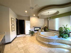 Primary bathroom featuring an inviting chandelier, a bathtub, and a multi sided fireplace