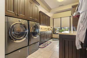 Clothes washing area featuring visible vents, independent washer and dryer, and cabinet space